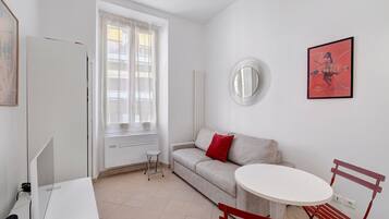 A modern, minimalistic room with a white sofa, a round mirror, a small round table, and a red chair.