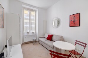 Ein modernes, minimalistisches Zimmer mit einem weißen Sofa, einem runden Spiegel, einem kleinen runden Tisch und einem roten Sessel.