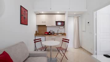 Ett kompakt bostadsutrymme med ett litet kök, en matplats med ett runt bord och stolar samt en soffa med en röd kudde.
