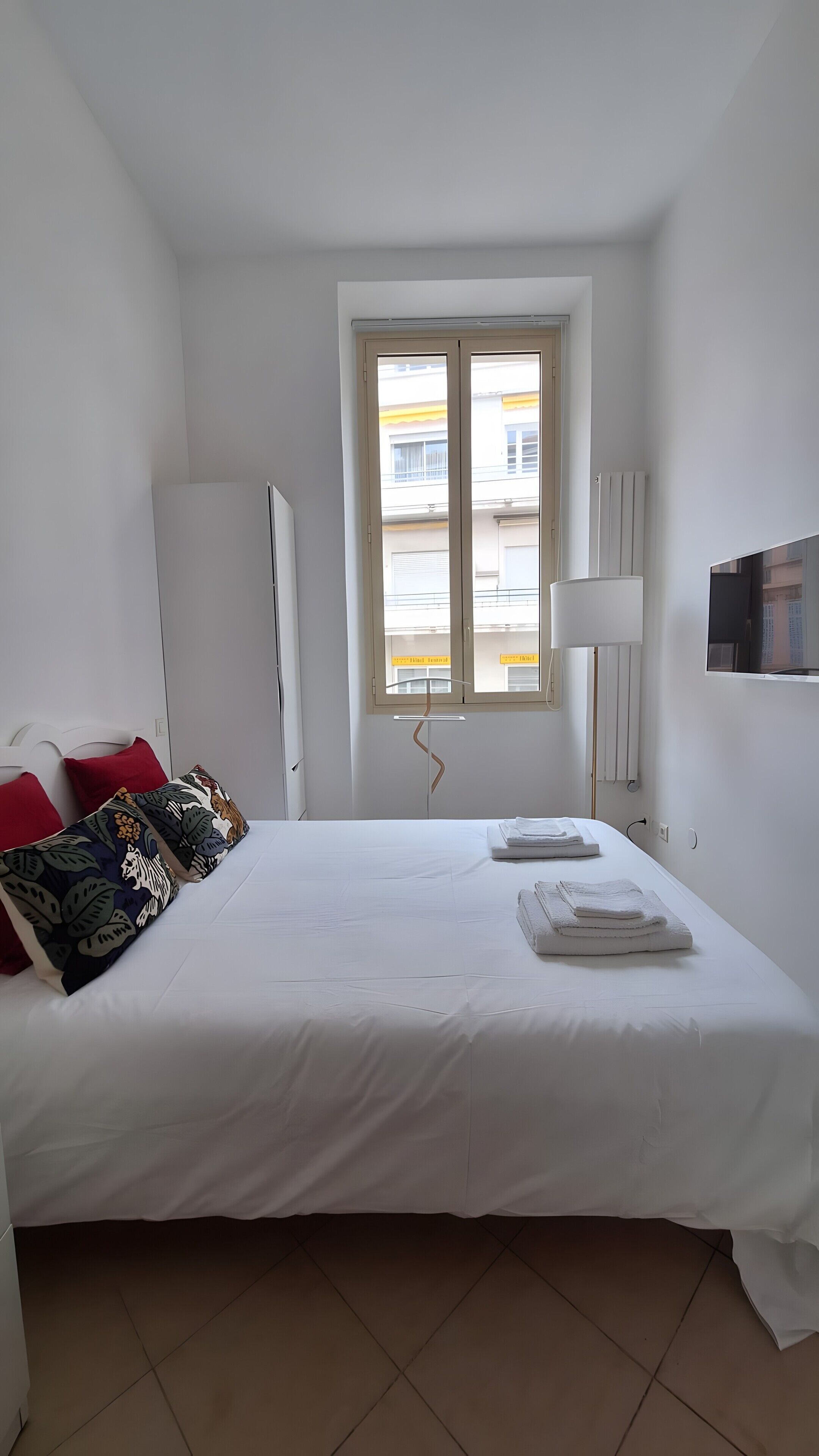 Ett hotellrum med en säng, ett fönster, ett skrivbord och en lampa.