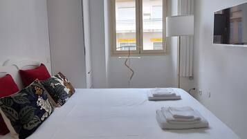 Una habitación de hotel con cama, ventana, escritorio y lámpara.