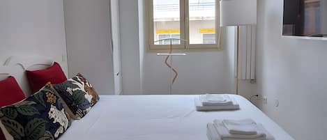 A hotel room with a bed, a window, a desk, and a lamp.