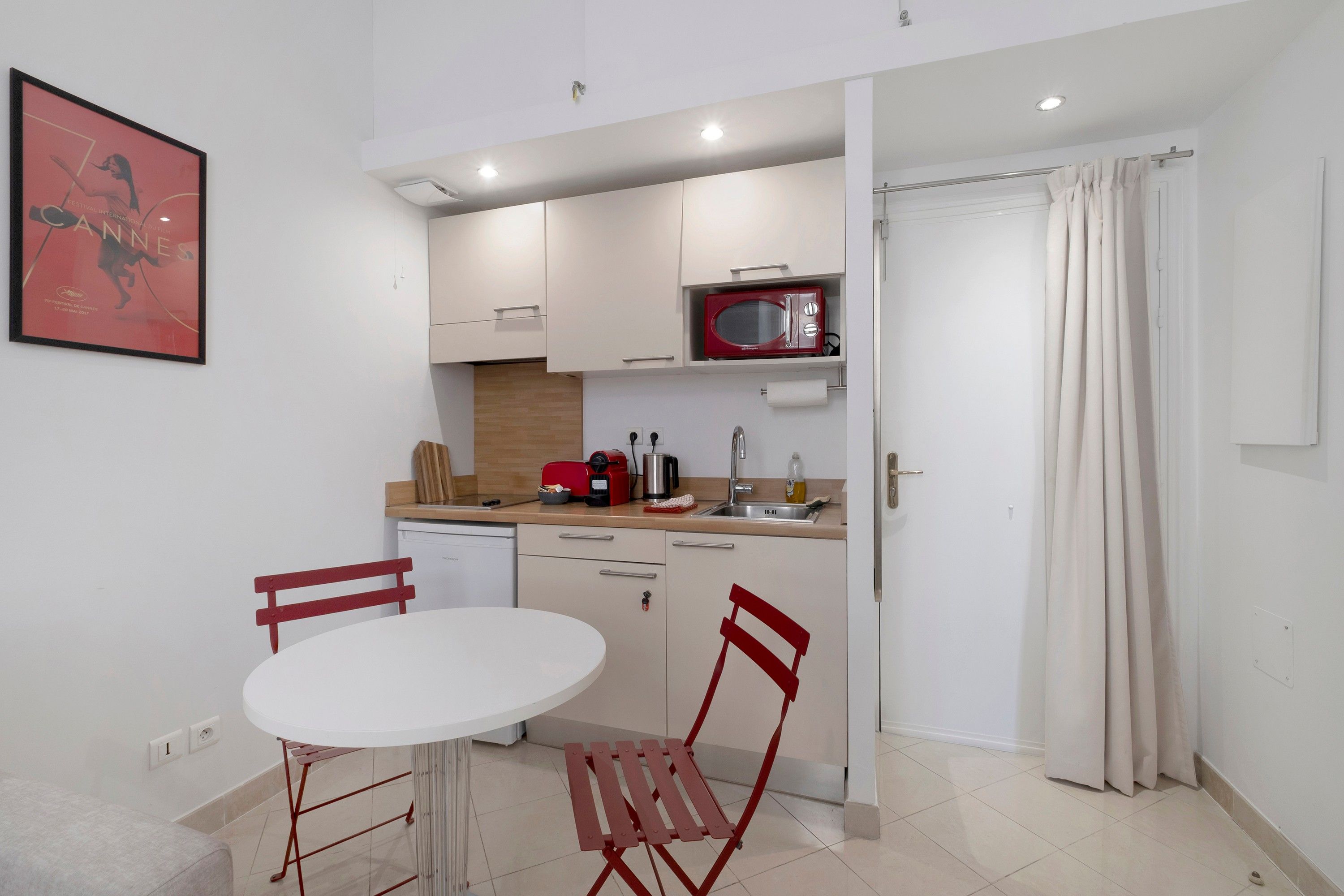 A compact kitchen with a white table and chairs, a red microwave, and a sink.