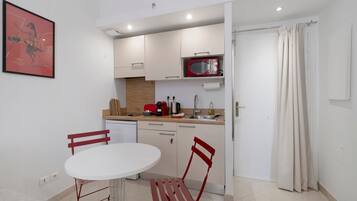 A compact kitchen with a white table and chairs, a red microwave, and a sink.