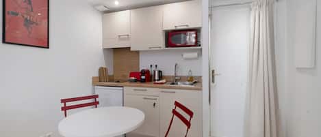 A compact kitchen with a white table and chairs, a red microwave, and a sink.