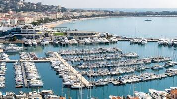 A marina with numerous boats docked, surrounded by buildings and a beach in the background.