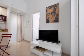 Ein modernes Wohnzimmer mit einem Flachbildfernseher auf einem weißen Schrank, einem roten Klappstuhl und einer Tür zu einem anderen Raum.