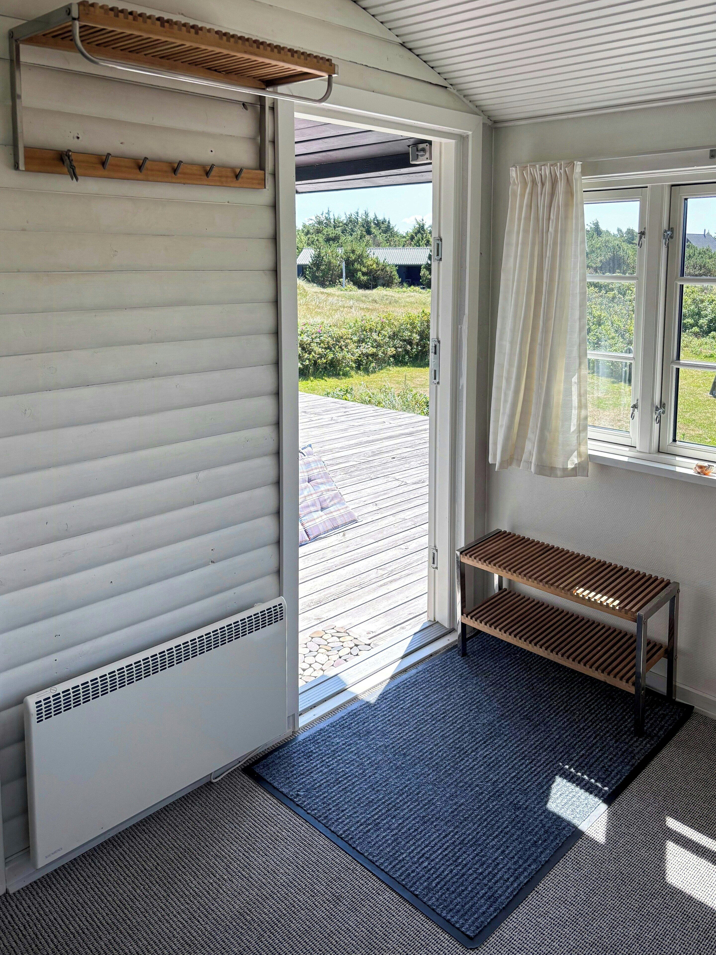 Une pièce avec un banc en bois, une fenêtre avec des rideaux et une vue sur un jardin.