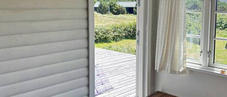 Une pièce avec un banc en bois, une fenêtre avec des rideaux et une vue sur un jardin.