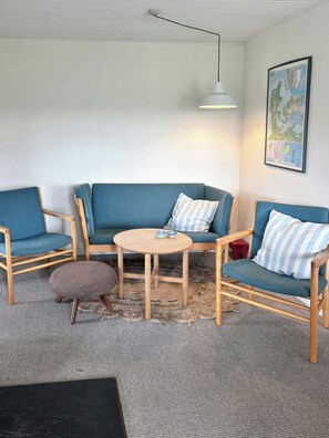 A living room with a blue sofa set, a round wooden coffee table, and a woven rug. - Summer house with wilderness bath near Henne (Oksbøl)