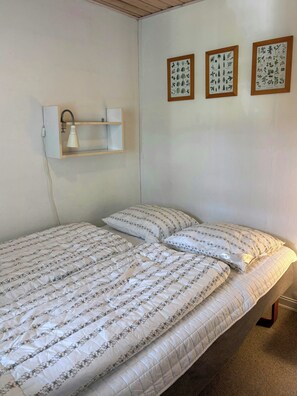 Ein Einzelbett mit einem blumigen Überwurf und Kissen, eine Nachttischlampe sowie drei gerahmte Pflanzenmotive an der Wand.
