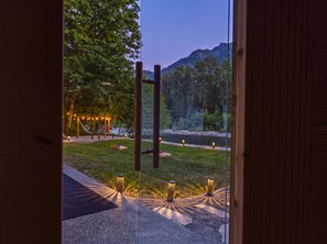 An outdoor patio with a hammock, string lights, and lanterns, overlooking a river and forested mountains. - Riverfront Resort w/ Spa~Firepit~Hammock~Theater~Games~Sleeps 20~Amazing Views (Gold Bar)