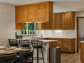 Eine moderne Küche mit Holzschränken, einer zentralen Kochinsel mit Barhocker und einem Edelstahlkühlschrank.