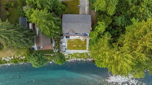 Ein Luftbild eines Hauses mit Rasen, Auffahrt und freiem Blick auf die umliegende Grünfläche und das Wasser.