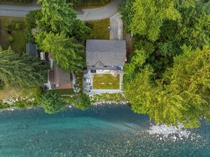 Ein Luftbild eines Hauses mit Rasen, Auffahrt und freiem Blick auf die umliegende Grünfläche und das Wasser.