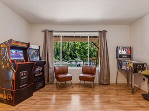 Ein Zimmer mit Holzboden, zwei Ledersesseln, einem Fenster mit Vorhängen und Spielautomaten.