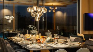 A modern dining area with a long table set for a meal, a chandelier, and a television mounted on the wall. - Luxury Villa Lara With Heated Pool, Hot-tub and Sauna - Six Bedroom Villa With Pool (Zmijavci)
