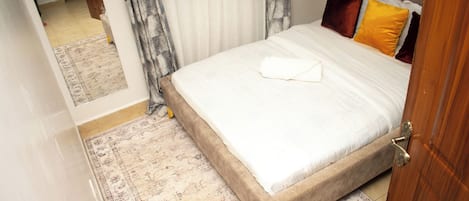 A neatly made bed with a white duvet, a brown headboard, and a variety of pillows.