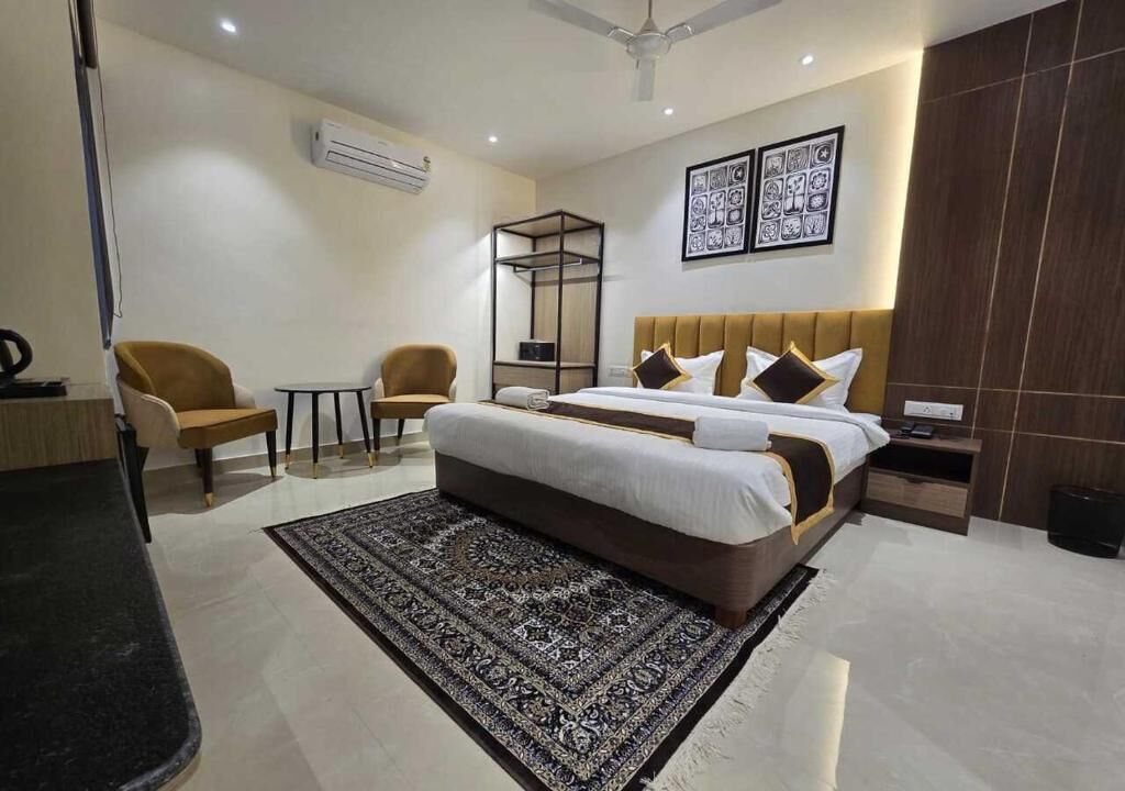 A hotel room with a large bed, two armchairs, a small table, a bedside table, a mirror, and a ceiling fan.