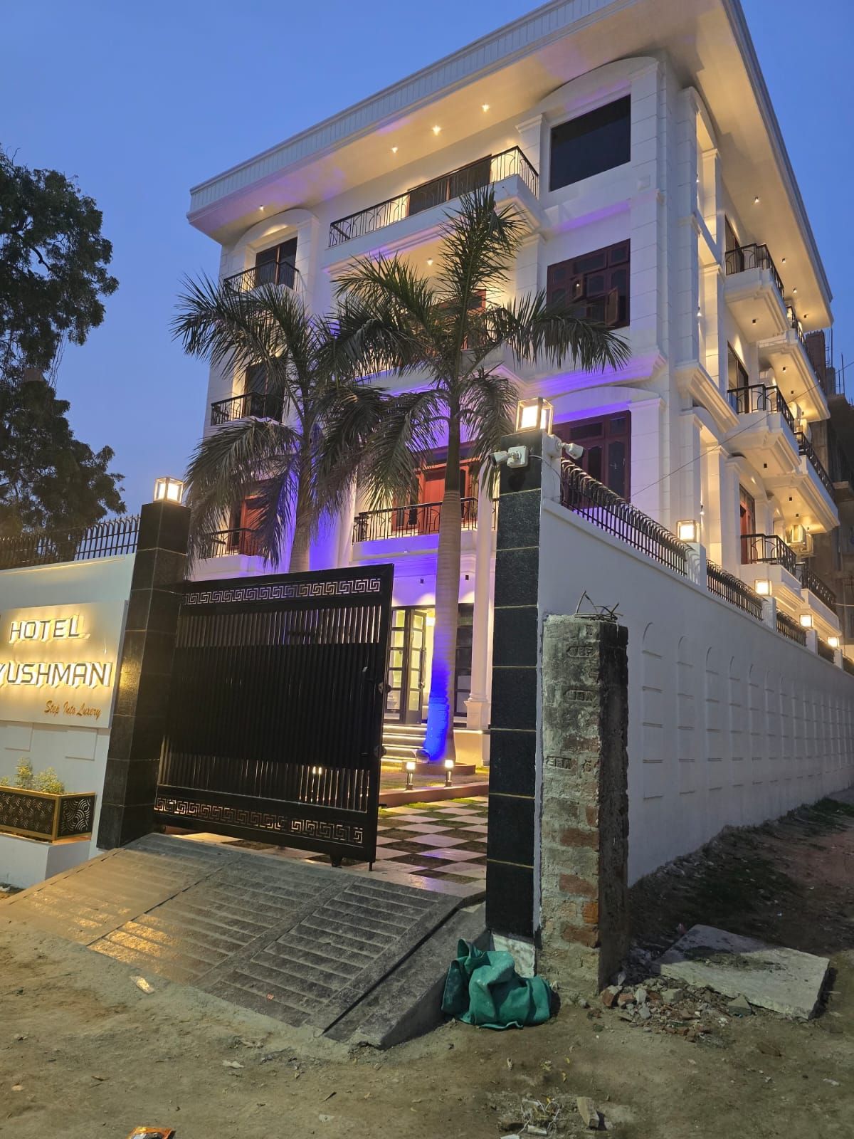 A multi-story hotel with a gated entrance, palm trees, and illuminated lighting.