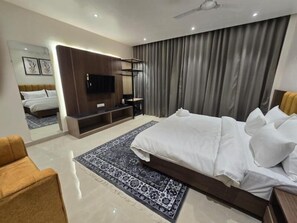 A modern hotel room with a large bed, a flat-screen TV, a seating area, and a large mirror. - HOTEL AYUSHMAN (VARANASI)