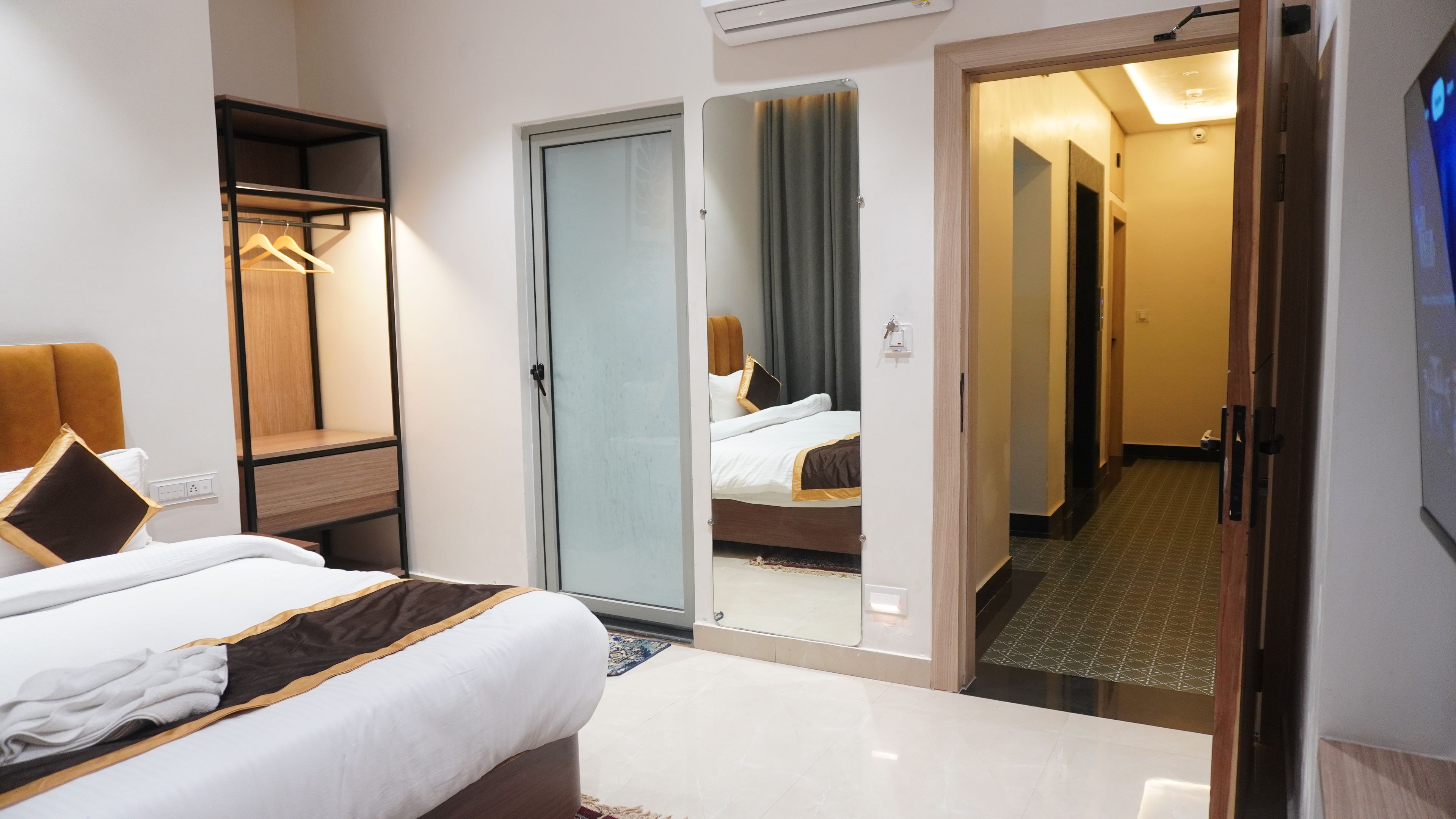 Ett hotellrum med en säng, en garderob, en spegel och en dörr som leder ut till en hall.
