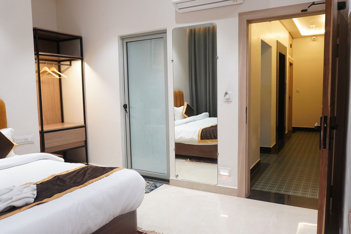A hotel room with a bed, a wardrobe, a mirror, and a door leading to another room.