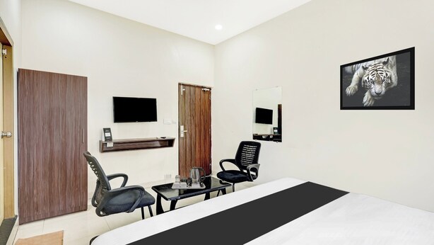 A hotel room with a bed, two chairs, a desk with a coffee maker, a flat-screen TV, and a framed picture on the wall. - OYO Collection O Dabagardens Near RK (Visakhapatnam)