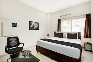 A hotel room with a bed, a chair, a small table with a coffee pot, a picture frame, and a window with curtains. - OYO Collection O Dabagardens Near RK (Visakhapatnam)