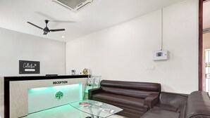 A reception area with a reception desk, a ceiling fan, a brown leather sofa, a glass coffee table, and a wall-mounted thermostat. - OYO Collection O Dabagardens Near RK (Visakhapatnam)