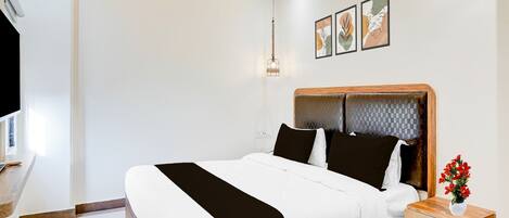 A modern bedroom with a wooden bed frame, white bedding, a bedside table with a vase of flowers, and a wall-mounted light fixture.