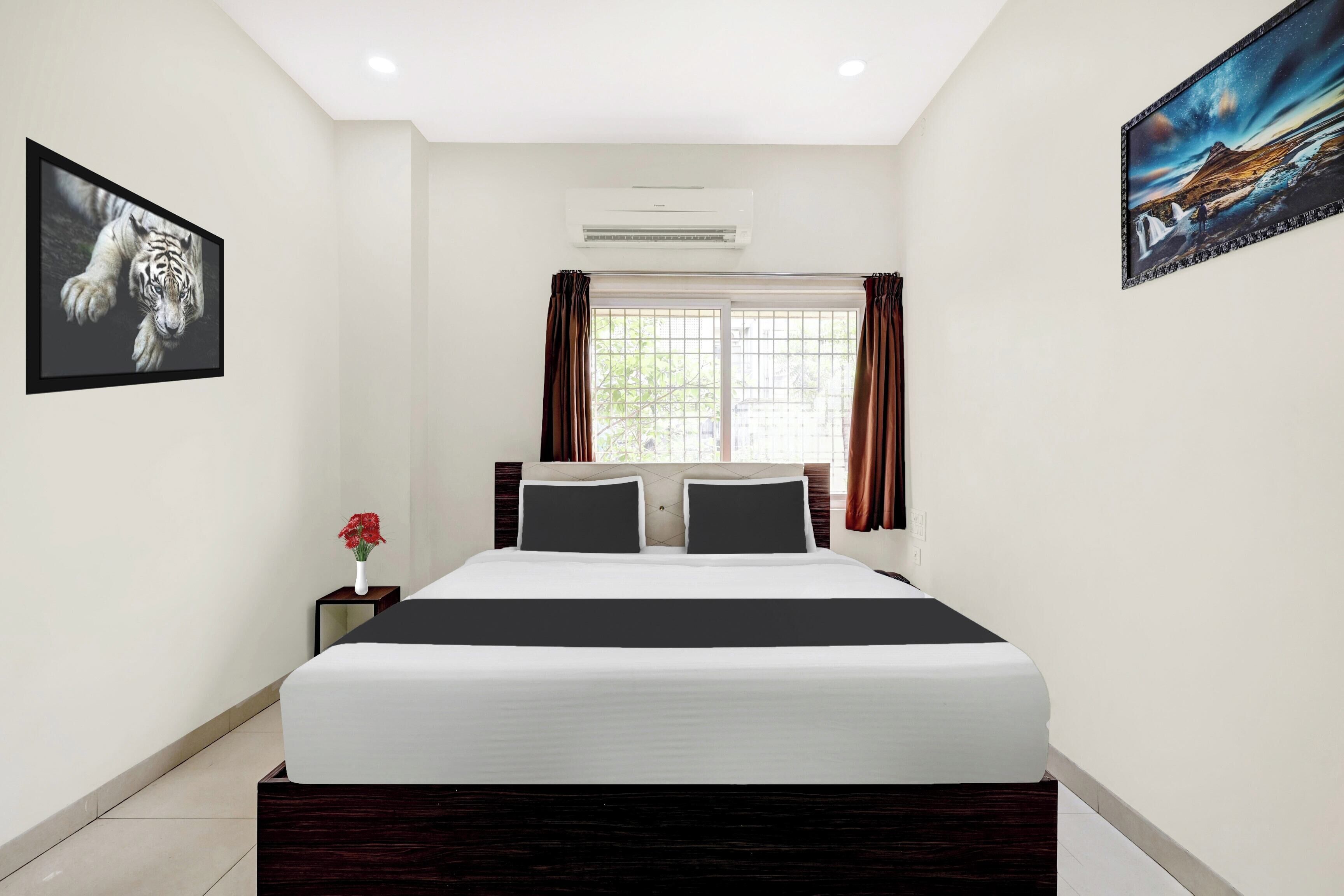 A hotel room with a bed, a nightstand, a vase of flowers, and two paintings on the walls.