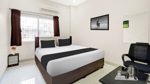 Une chambre d’hôtel avec un lit, une chaise, une table basse et une fenêtre avec des rideaux.