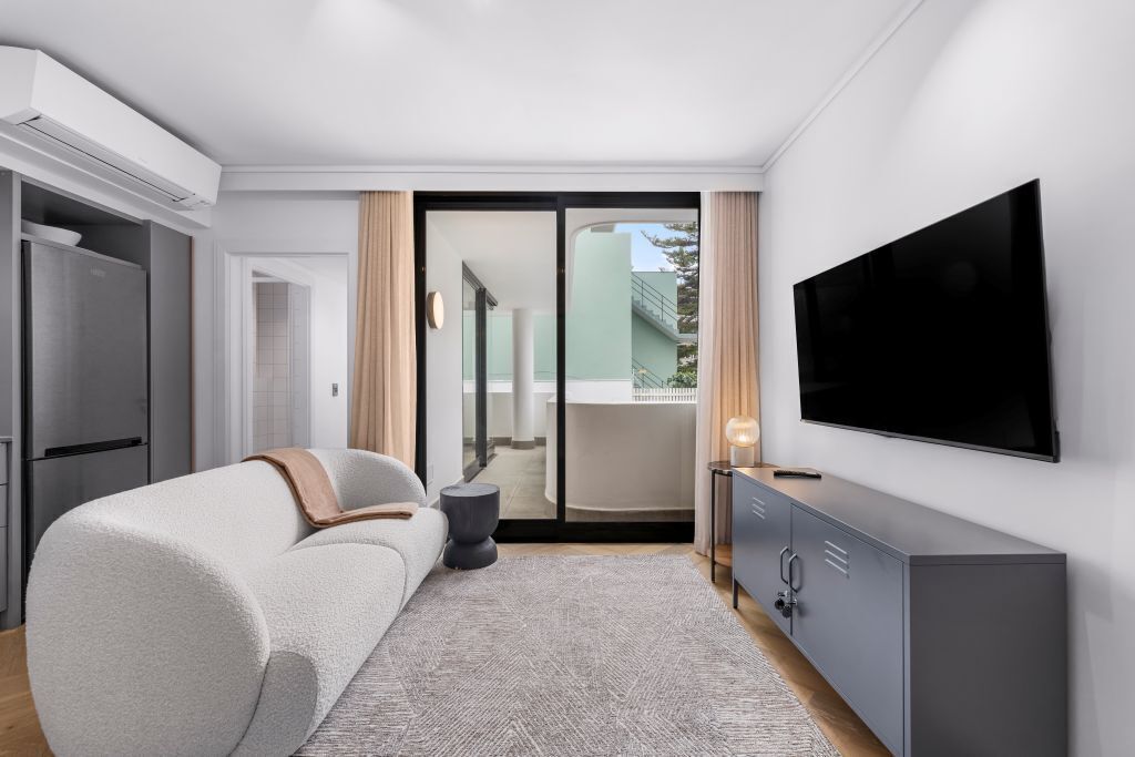 A modern living room with a sofa, a flat-screen TV, and a sliding glass door leading to an outdoor balcony.