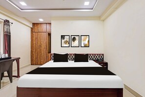 Habitación de hotel con una cama grande, un armario de madera, una mesita de noche y tres cuadros enmarcados en la pared.