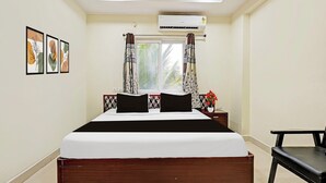 A hotel room with a bed, a window with curtains, an air conditioning unit, and framed artwork on the wall. - Super Collection O Beach Road Near GITAM (Visakhapatnam)