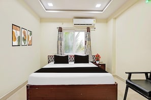 Una habitación de hotel con cama, ventana con cortinas, aire acondicionado y cuadros en la pared.