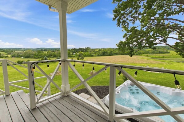 A wooden deck with a hot tub and string lights, overlooking a green landscape.