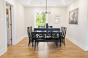 A dining area with a black table and chairs, a chandelier, and a window with blinds. - Greystone Lavender Farm-Hot Tub|Pool Table|KoiPond (Meaford)