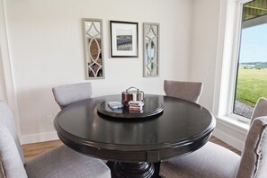 A round table with four chairs, a framed picture, and a window with a view of a field.