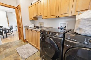 A kitchen with wooden cabinets, a washing machine, and a granite countertop. - Greystone Lavender Farm-Hot Tub|Pool Table|KoiPond (Meaford)