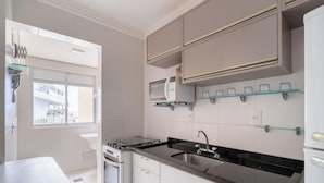 A modern kitchen with a gas stove, a sink, and a built-in oven. There are cabinets above the counter and a window with blinds. - Apartment With Balcony and Barbecue Cac0109 (Florianópolis)