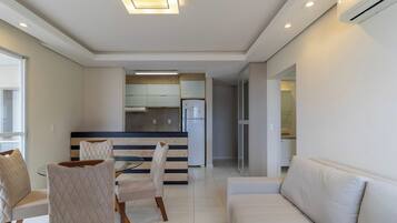 A modern living room with a sofa and chairs, a dining area with a table and chairs, and a kitchen with a refrigerator and cabinets.