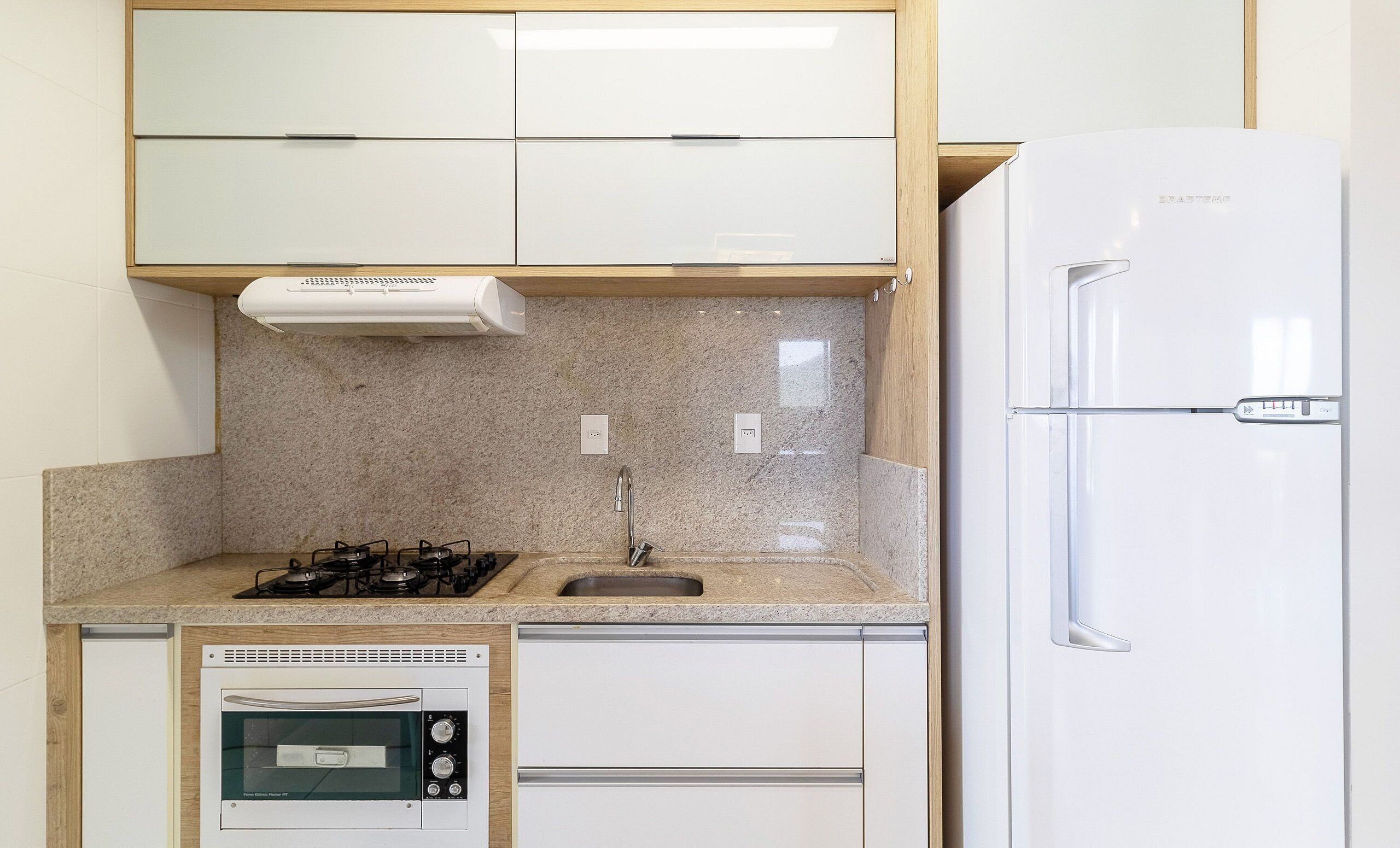 Une cuisine compacte équipée d’un four encastré, d’une cuisinière à gaz, d’un évier et d’un réfrigérateur.