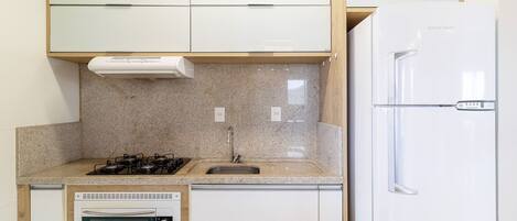 Cocina compacta con horno integrado, cocina a gas, lavamanos y refrigerador.
