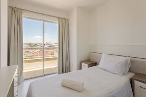 Une chambre d’hôtel avec un lit, une table de chevet, un bureau et une vue sur les bâtiments, visible à travers une grande fenêtre.