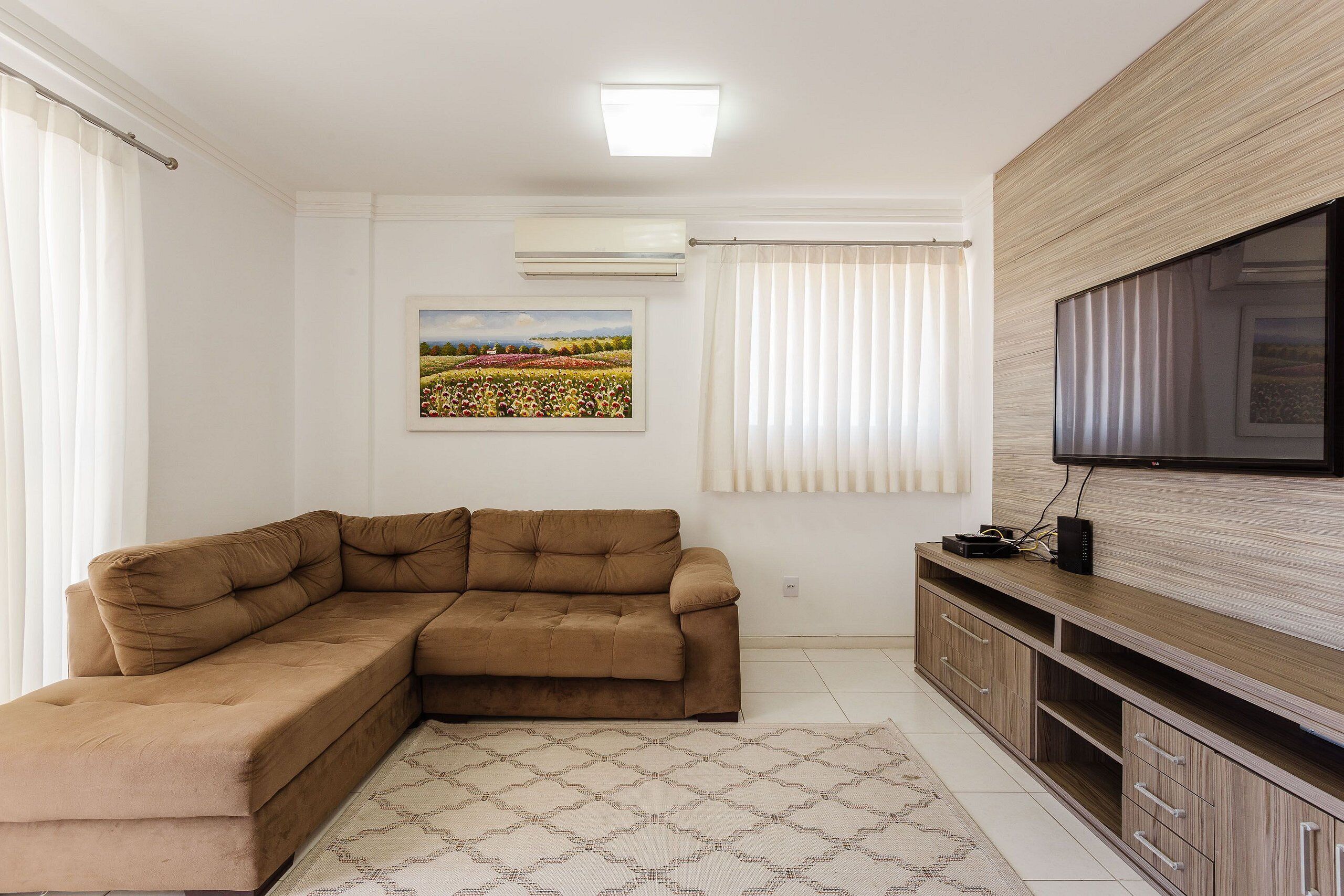 A living room with a sectional sofa, a flat-screen TV, a wooden cabinet, and a patterned rug.