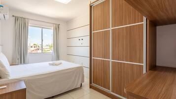 Habitación de hotel con cama, armario de madera, escritorio y ventana con cortinas.