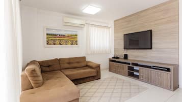 Una sala de estar con un sofá seccional, un televisor de pantalla plana, un mueble de madera y una alfombra estampada.