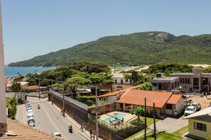 Un quartier résidentiel doté d’une piscine, d’une rue bordée de voitures garées, et offrant une vue sur la mer et les collines.